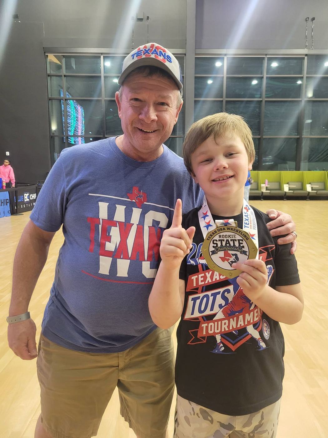 Warren holding up one finger with his state championship medal, next to Coach Nick McClellan